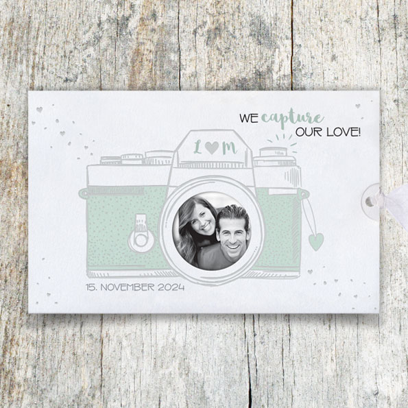 Vergrößerte Abbildung Fotokarte mit im Comicstil gezeichneter Kamera. Im Objektiv ist eine Abbildung des Brautpaares abgedruckt.