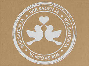 Vergrößerte Abbildung Weißer Stempelabdruck auf braunem Kraftkarton, den Schriftzug wir sagen ja, sowie zwei turtelnde Tauben mit weißem Herz darstellend.