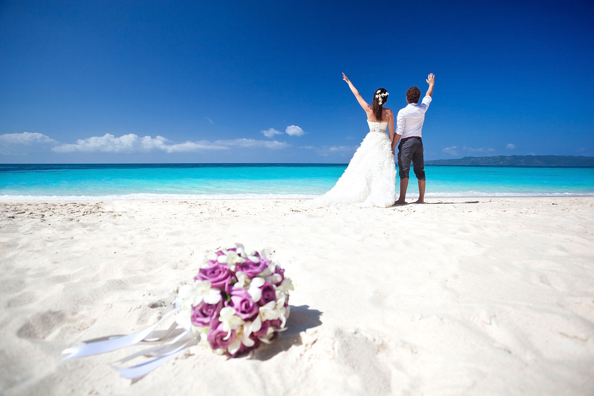 Hochzeitspaar am weißen Strand vor blauem Himmel.